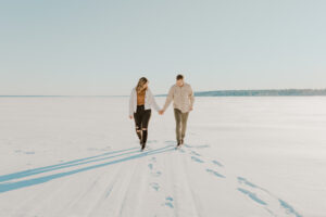 Engaged couple walks through open snowy landscape during their winter engagement session in Houghton Michigan
