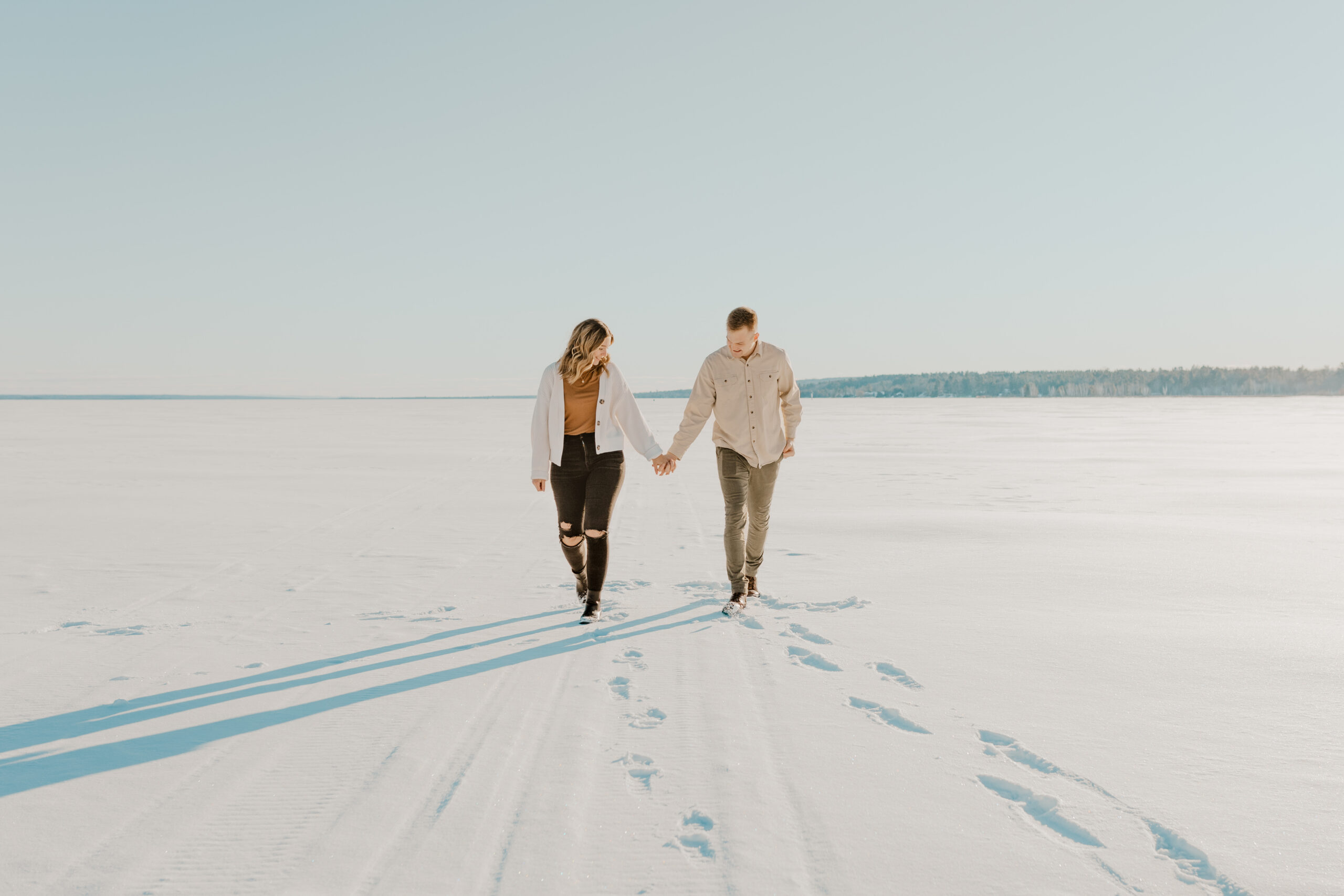 Engaged couple walks through open snowy landscape during their winter engagement session in Houghton Michigan